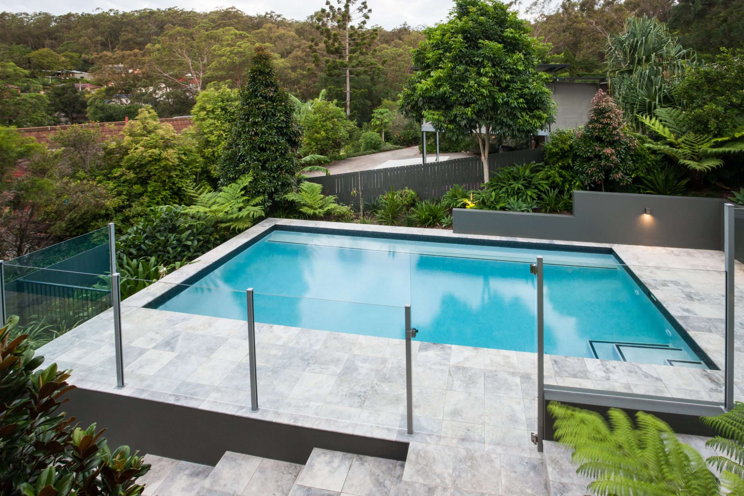 Modern backyard pool with glass fence and trees
